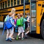 group of small kids with backpacks lined up outside a school bus. Feature image for an article on 4 Ways to Save Your Sanity In a New School Year