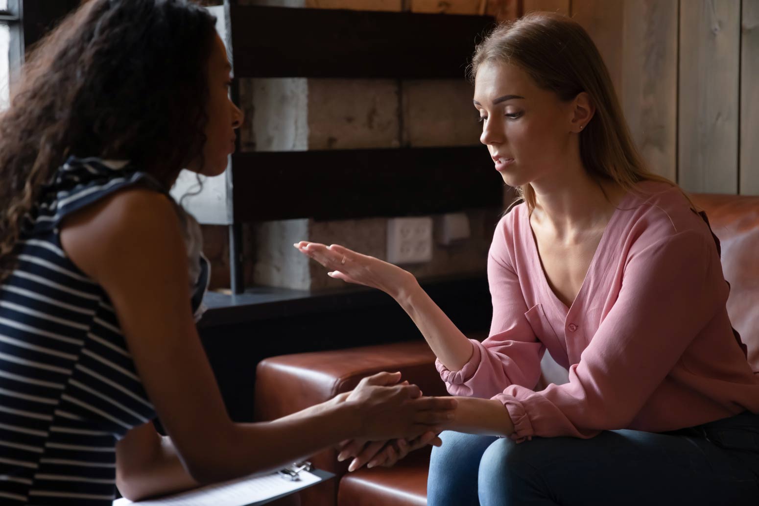 two women sitting across from each other, one holding the other's hand. Feature image for 5 Ways You can Help Loved Ones Struggling with Addiction