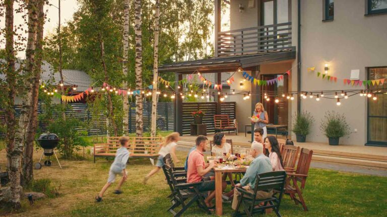 a group of people eating at a table together in the backyard of a home; a lesson in how to become friends with your neighbors