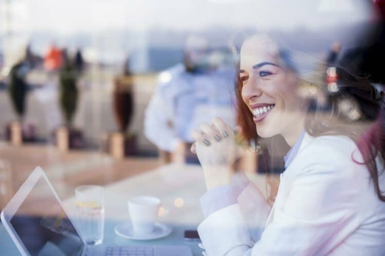 woman who learned how to overcome feeing nervous as a leader behind a cafe window smiling with hands clasped