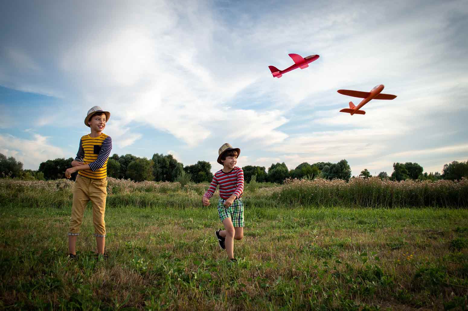 two boys in a grassy field throwing toy airplanes. Feature image for the article titled Old School Parenting Makes Happier Kids—and Moms