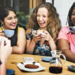 a group of racially different women laughing and drinking tea together as an act of forming a unified world