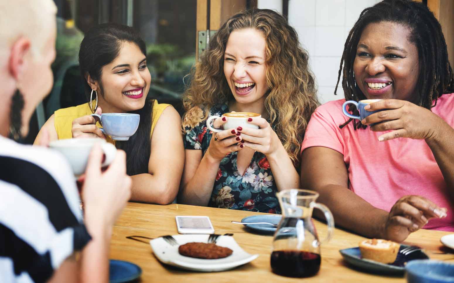 a group of racially different women laughing and drinking tea together as an act of forming a unified world