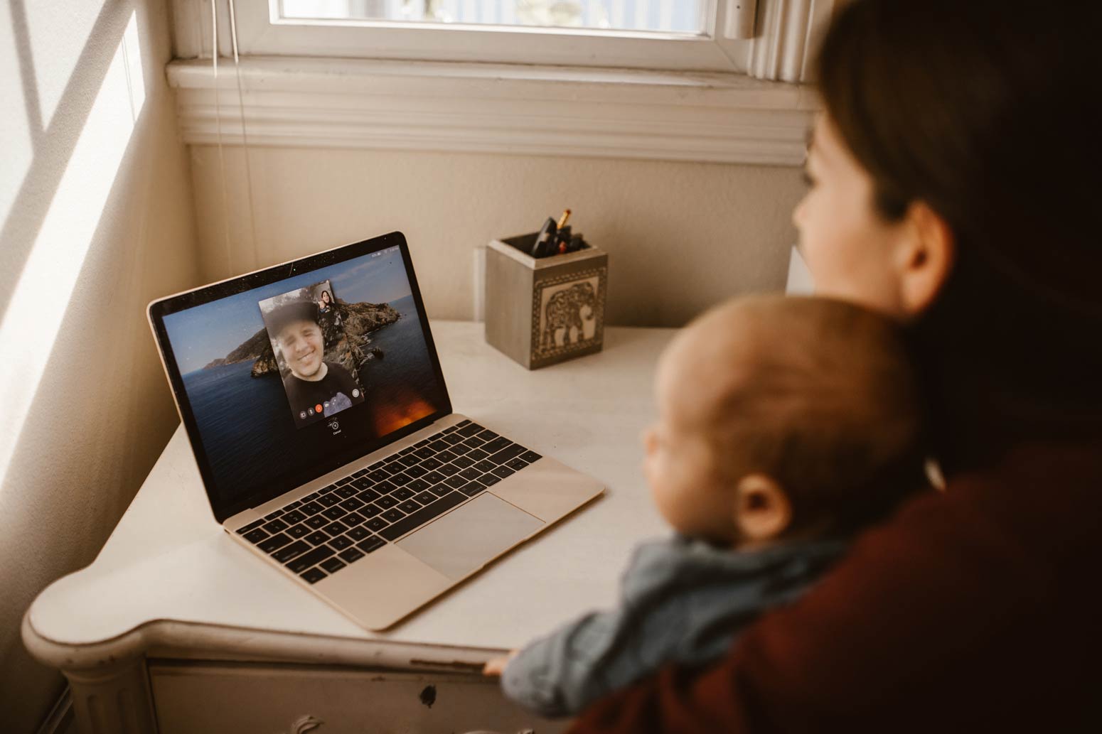 mom and baby talking to dad via facetime on a laptop. Feature image for 5 Ways to Stay Connected When a Family Member Is Traveling