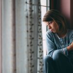 one woman who is feeling the loneliness epidemic gazes out a window looking sad
