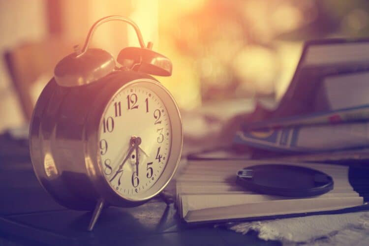 alarm clock on a nightstand next to a stack of reading material. Feature image for Stuck In Shame? Find Freedom from Your Past!