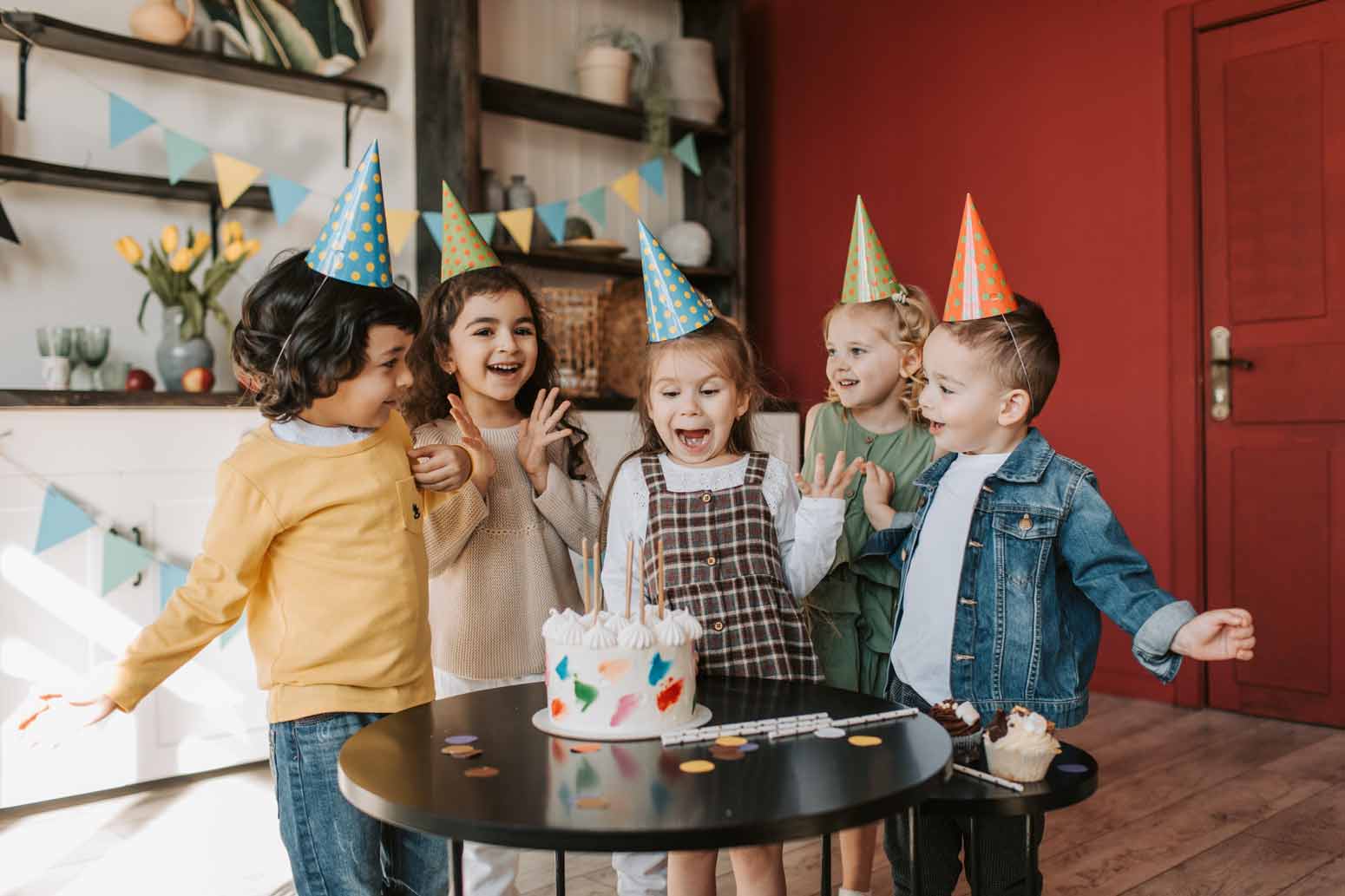 excited young children smiling and laughing in front of a birthday cake. Feature image for Ever Crash a Kid's Birthday Party? I Did and I’m Still a Good Mom