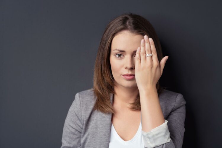 brunette woman holding up her hand to cover half her face to hide that she's not perfect