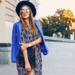 fashionable woman in a dress with a blue coat over her shoulders and sunglasses and a hat embodies the art of dressing for yourself
