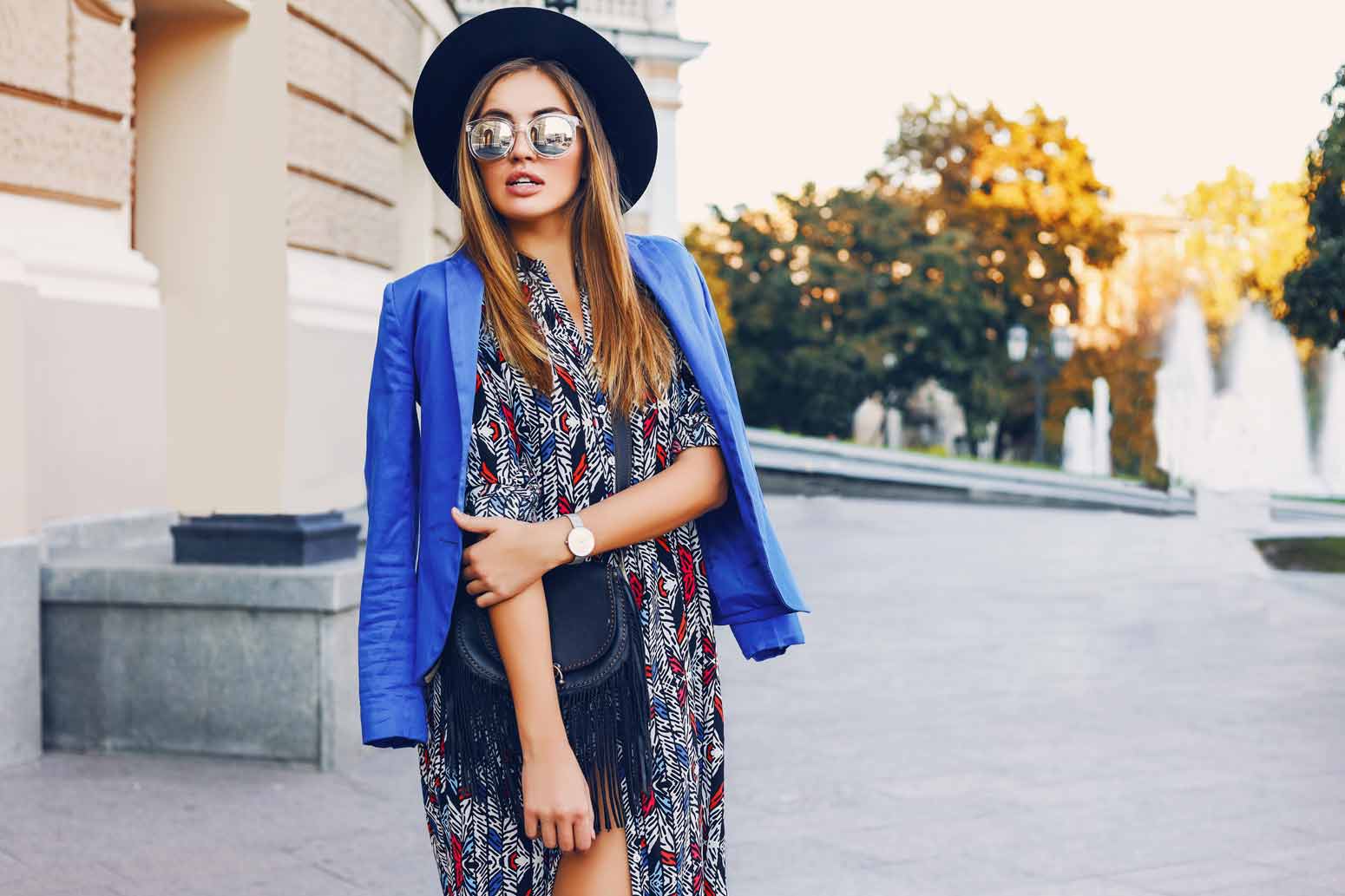 fashionable woman in a dress with a blue coat over her shoulders and sunglasses and a hat embodies the art of dressing for yourself