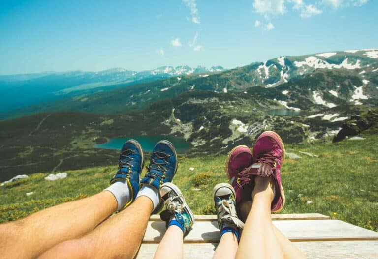 view of family's sneaker-covered legs lined up next to each other with a vast mountain landscape background while visiting travel destinations in the U.S.