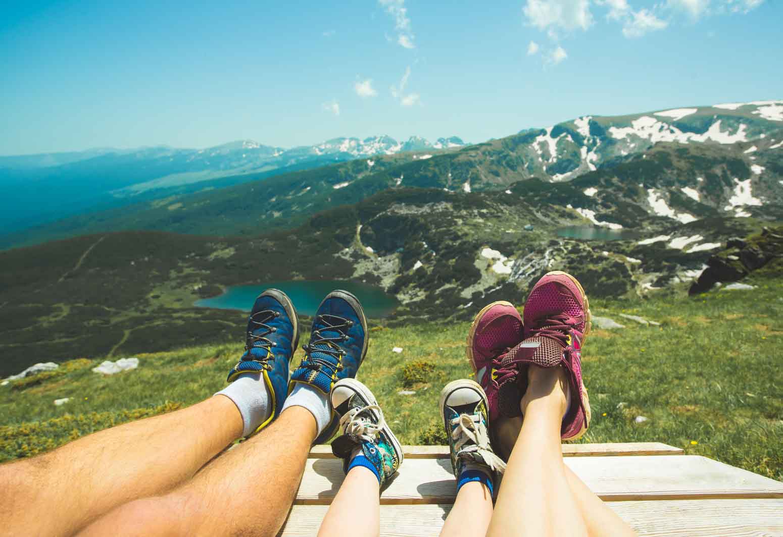 view of family's sneaker-covered legs lined up next to each other with a vast mountain landscape background while visiting travel destinations in the U.S.