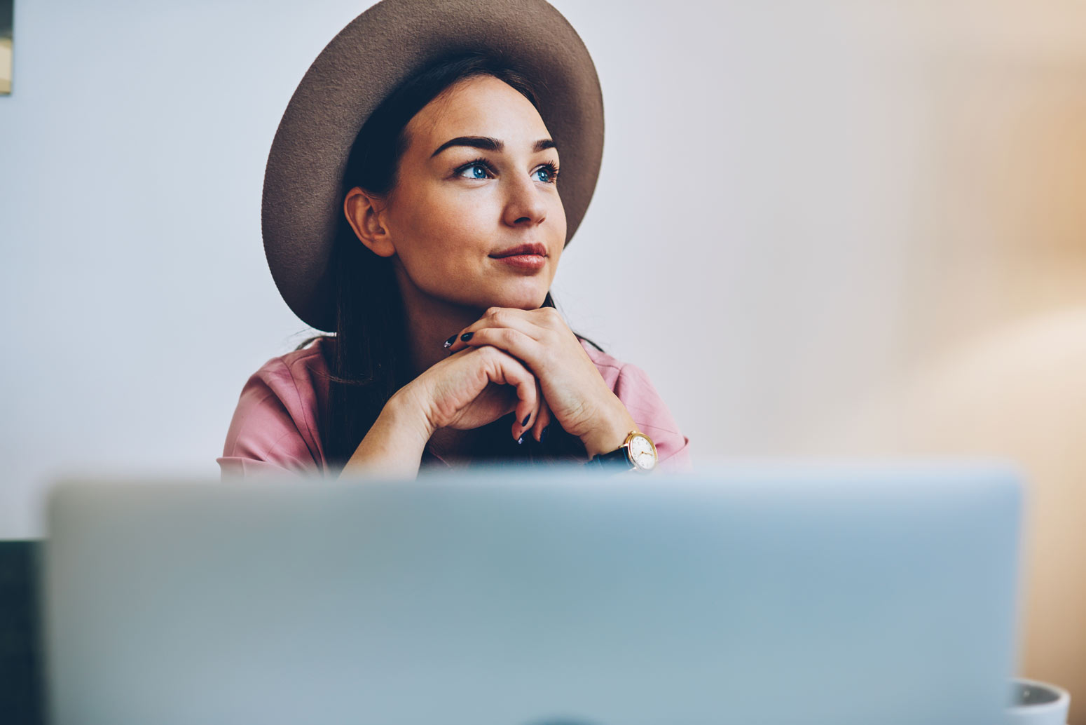 woman with hat looking thoughtfully over the top of her laptop with her chin resting on her hands wondering if she's wasting time trying to be perfect