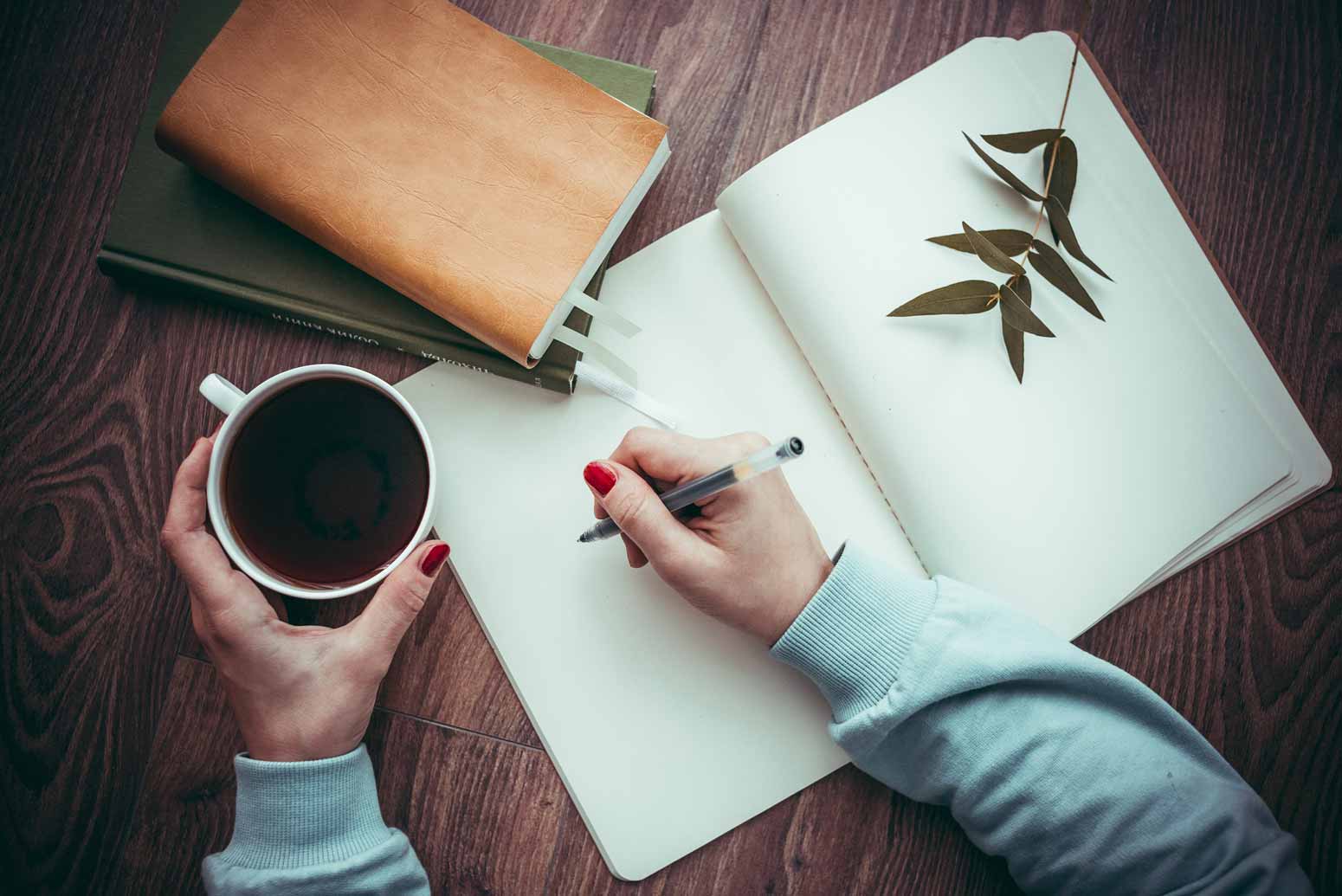 overhead view of a woman holding a cup of coffee while writing in a 30-day gratitude challenge journal with the other hand