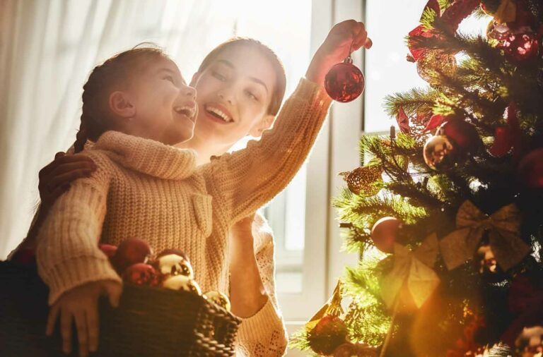 mom helping little girl put christmas tree ornaments on their tree