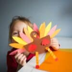 little girl holding up a colorful construction paper turkey for thanksgiving as a sweet gesture amid the mayhem of motherhood