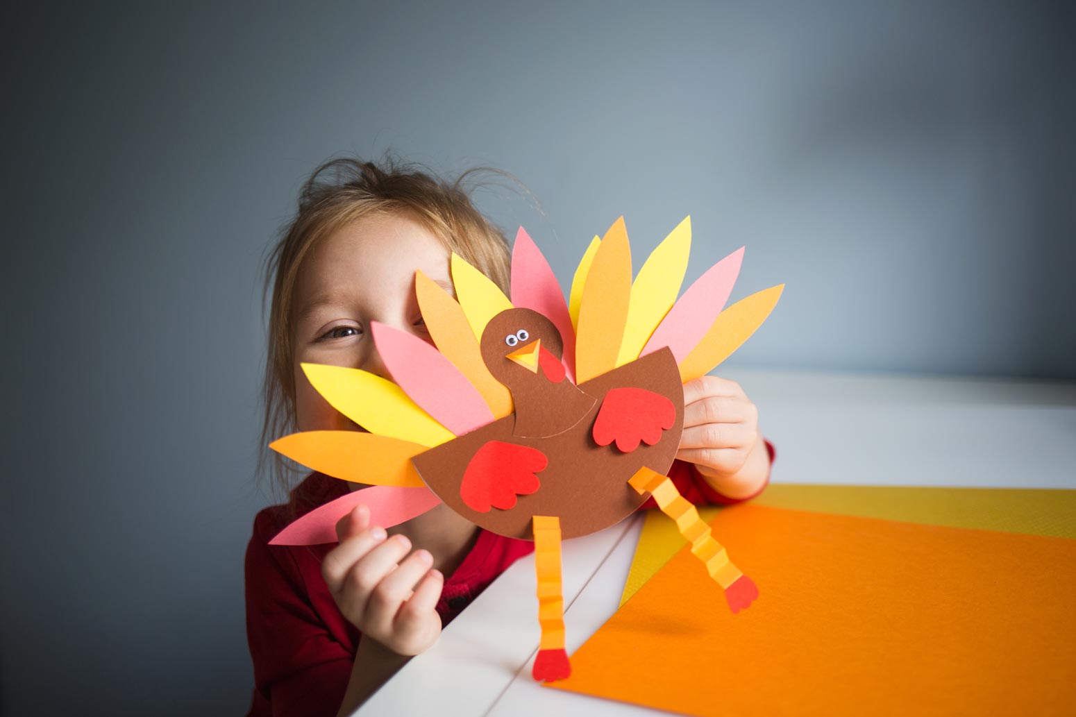 little girl holding up a colorful construction paper turkey for thanksgiving as a sweet gesture amid the mayhem of motherhood