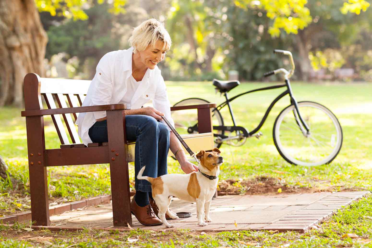 older woman sitting on a park bench and petting a small dog as a way to find joy in the everyday