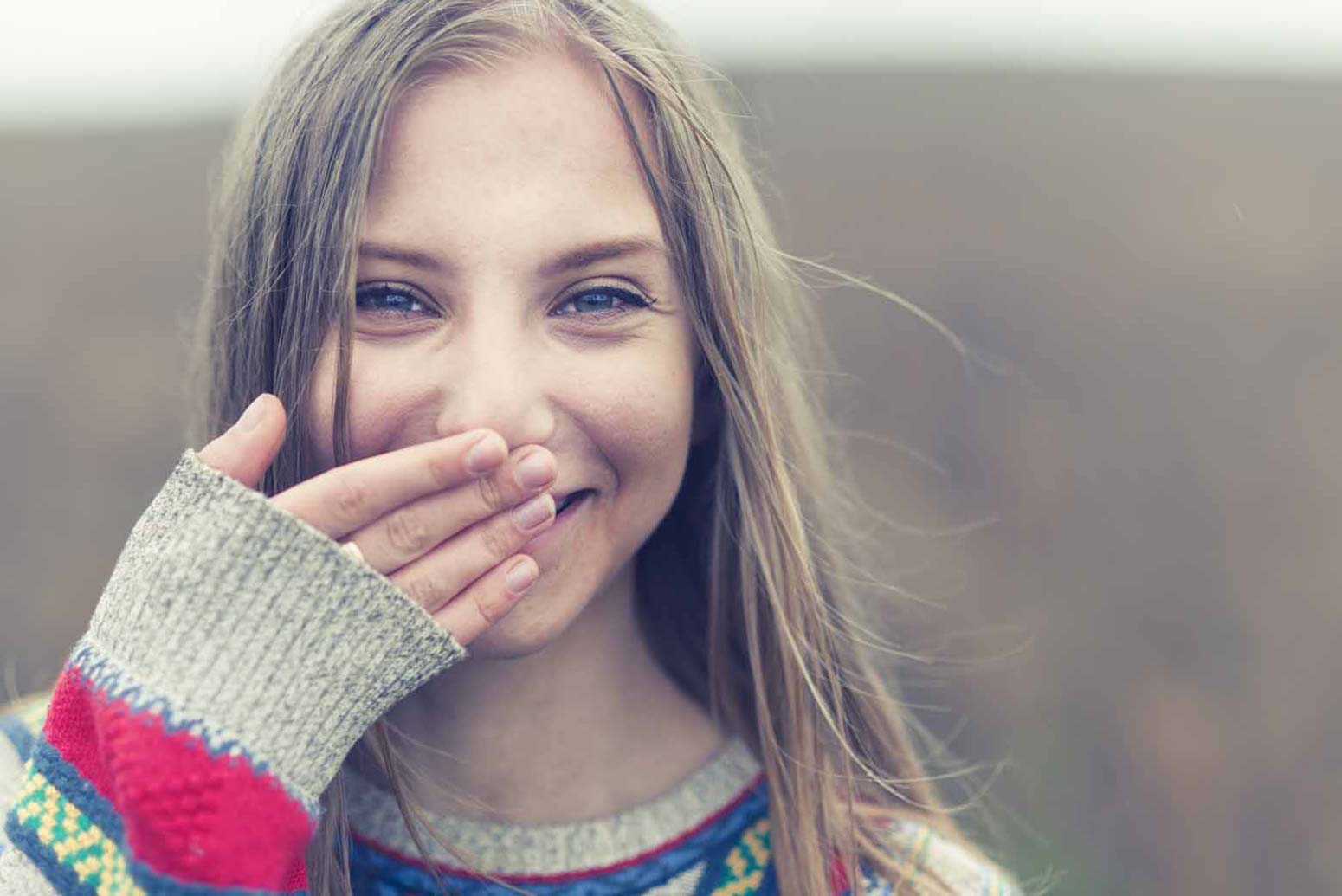 young girl smiling with hand covering her mouth