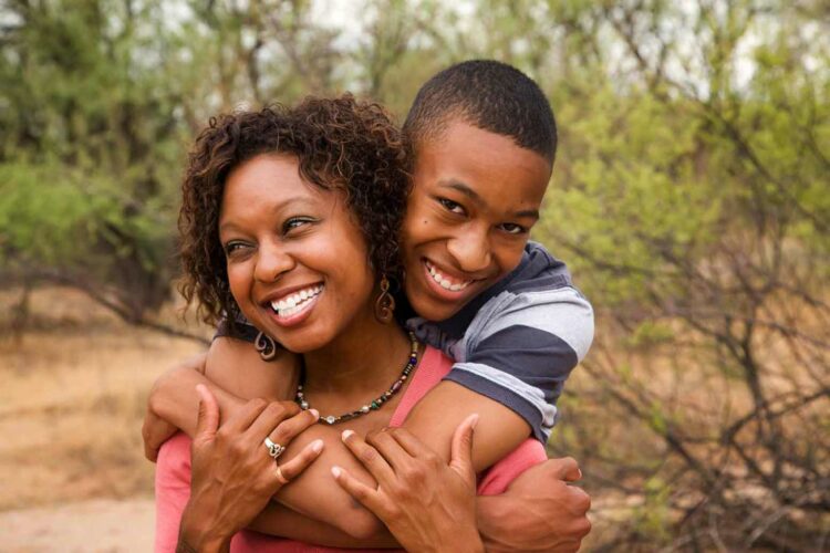 teenage son hugging mother from behind outside