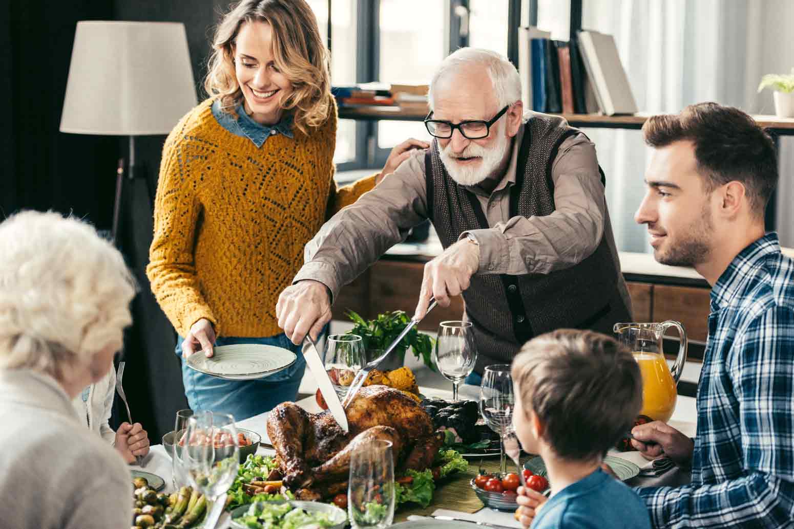 family members of different ages gathered around a table for Thanksgiving and the grandfather carving the turkey, exemplifying the power of intergenerational relationships