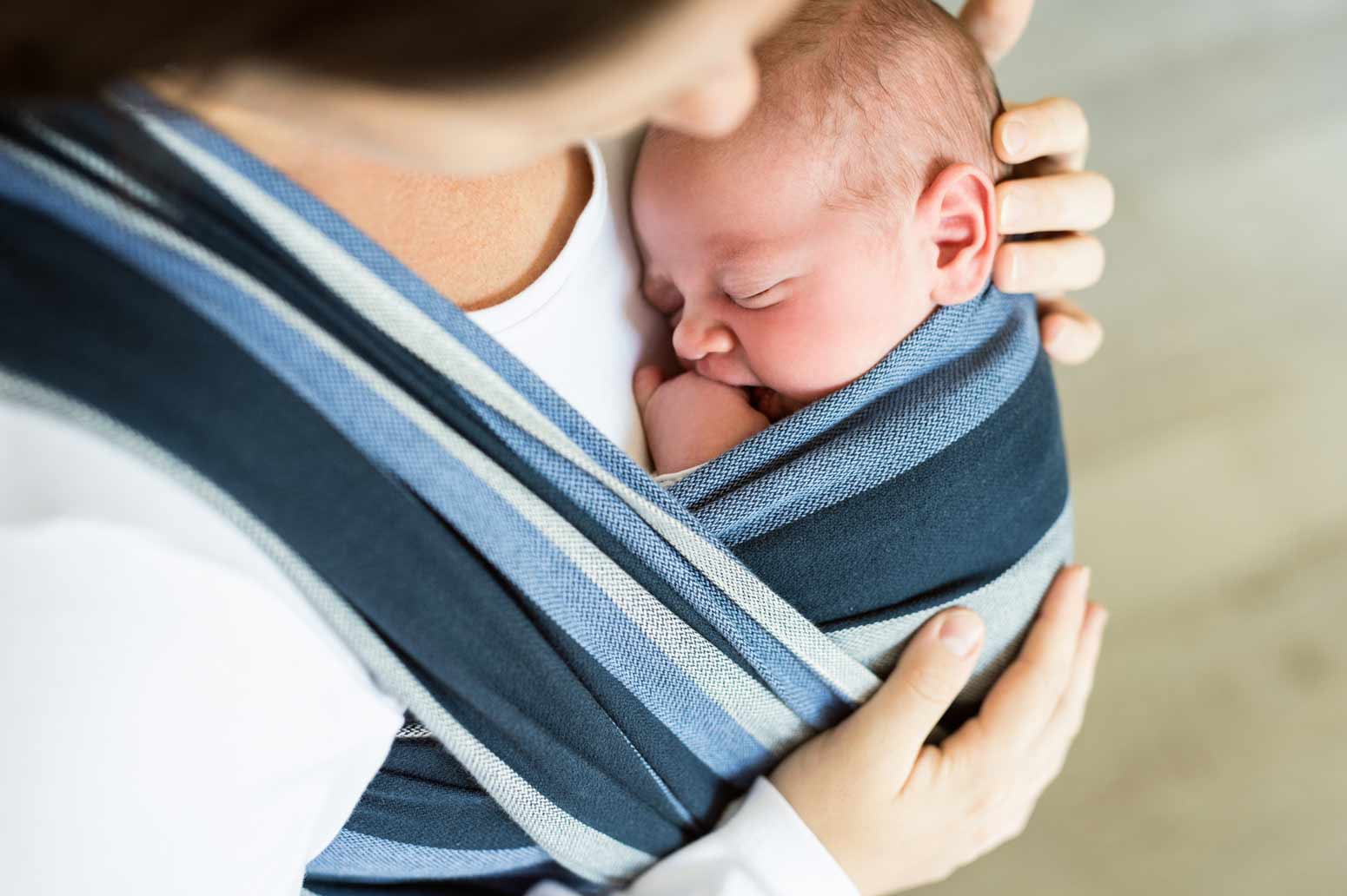 newborn baby attached to mother's chest in a blue sling, one of the joys of being a new mom