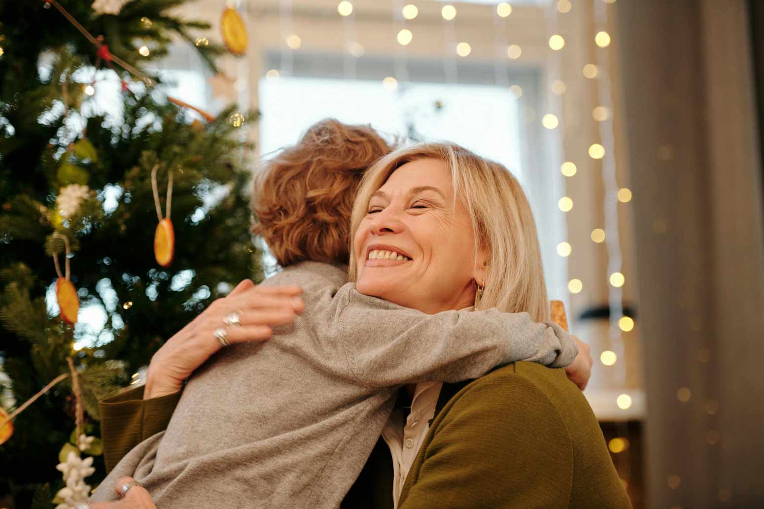 grandma hugging her son in front of a Christmas tree