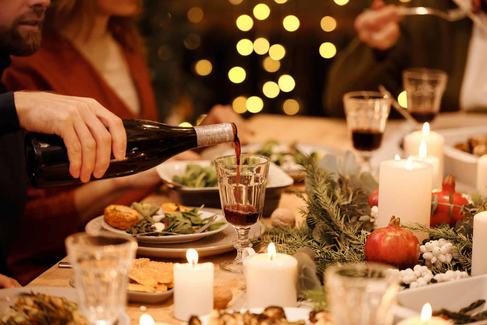 man pouring wine into a glass on a holiday dinner table, a potential dilemma for those needing a sober holiday survival guide