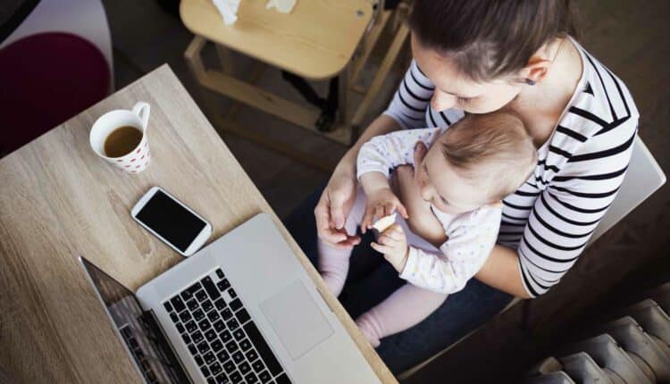 mom holding infant in her lap while working at her computer and wondering "who am I?"