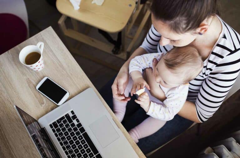 mom holding infant in her lap while working at her computer and wondering "who am I?"