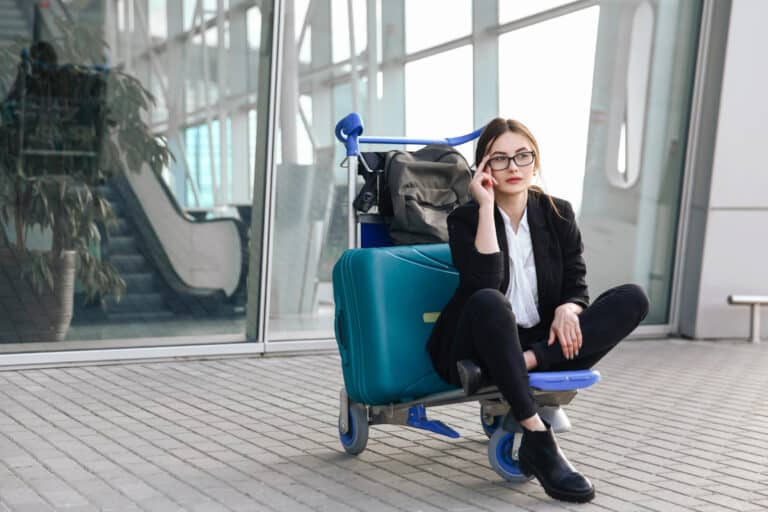 girl sitting next to luggage outside of the airport looking thoughtful and wondering what happens when your life change affects those you love