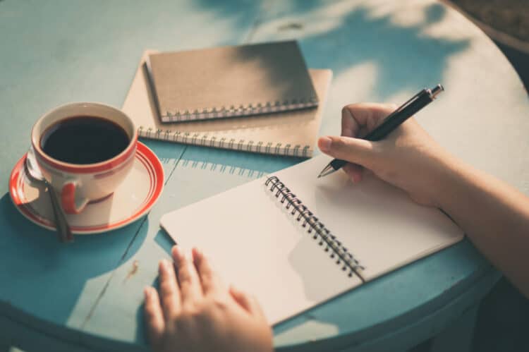 table view of a woman writing in a journal with a cup of coffee after choosing to forget new year's resolutions