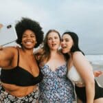 three happy women in bathing suits taking a selfie on the beach and not worried about body image issues