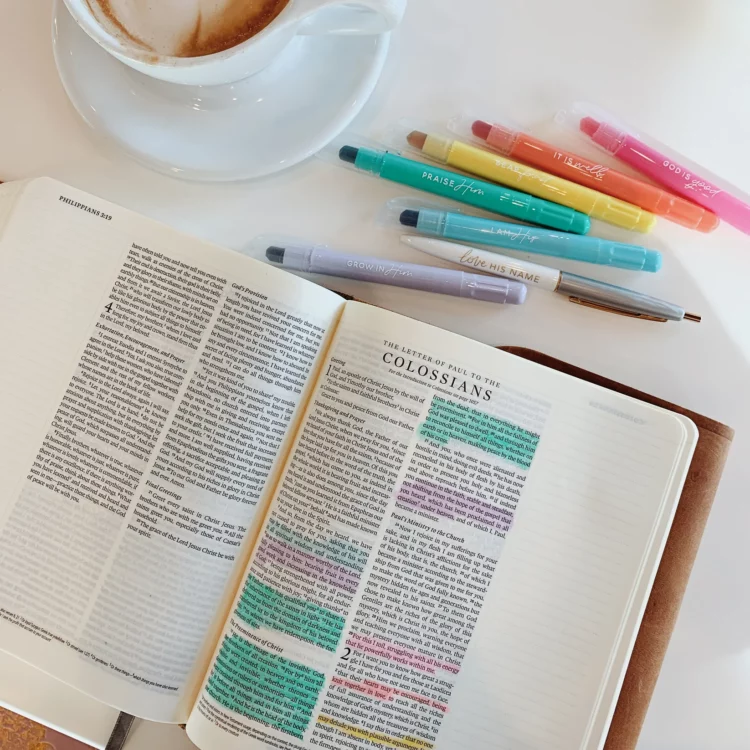 open Bible next to colorful highlighters and a cup of coffee