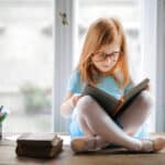 little girl sitting on top of a desk reading a Bible as an example of a way to grow your family's faith