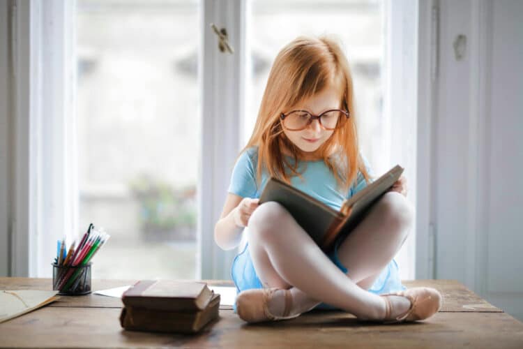 little girl sitting on top of a desk reading a Bible as an example of a way to grow your family's faith