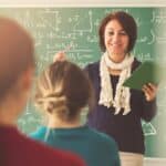 teacher standing in front of a chalkboard and smiling at her students