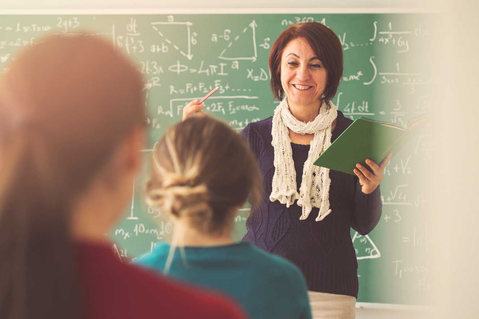teacher standing in front of a chalkboard and smiling at her students