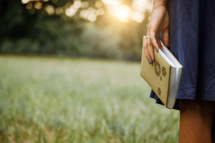 girl holding a journal at her side and standing in a field connecting the God dots in her life
