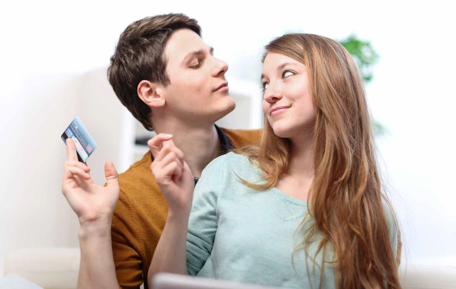 young man who learned to navigate love and finances playfully holding credit card away from smirking young woman