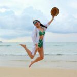 woman jumping in the air at the beach who is happy with her body image and swimsuits in the summer