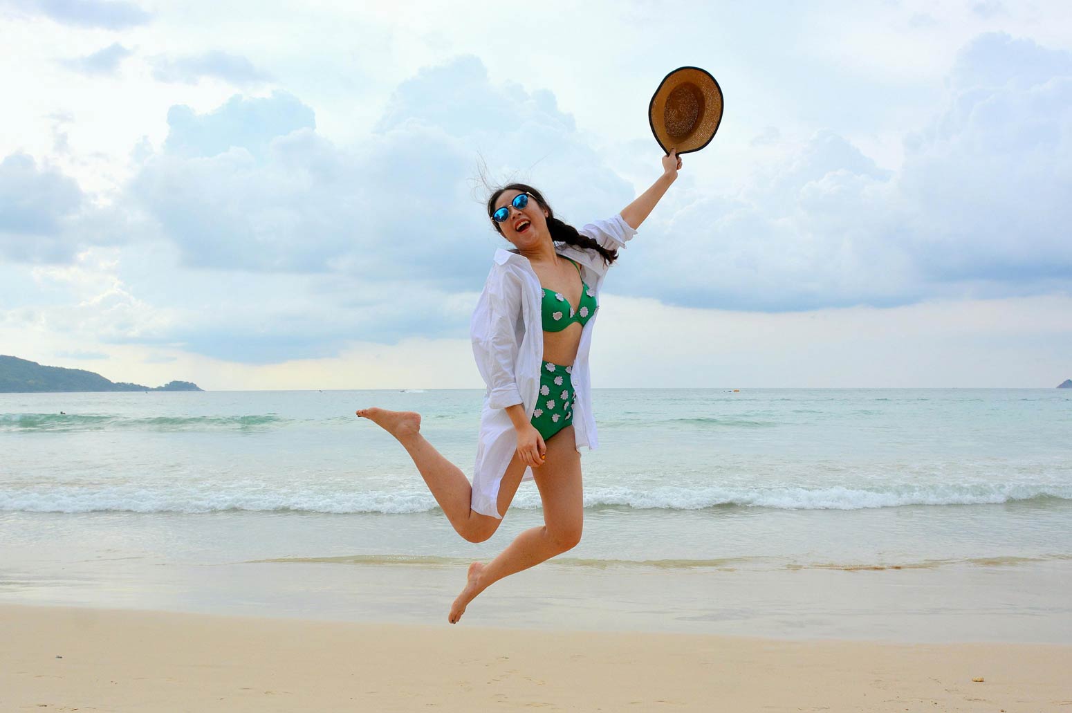 woman jumping in the air at the beach who is happy with her body image and swimsuits in the summer