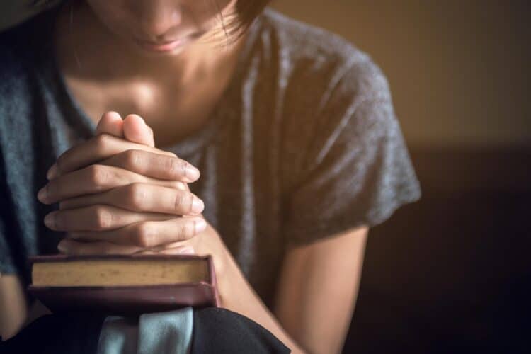 woman praying with hands clasped over a Bible after hearing Holy Spirit whispers