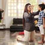 a mom kneels on the floor and measures her son's growth against a door frame since he's been experiencing growing pains
