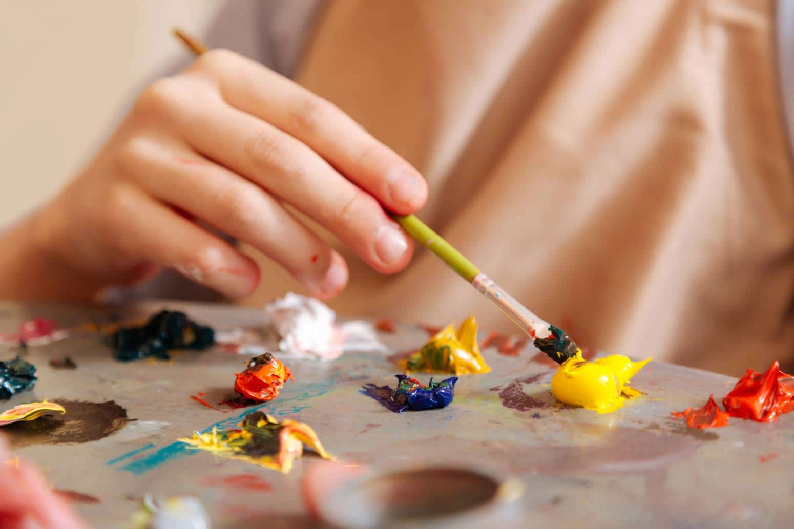 close-up of a woman grasping a paint brush above a palette of paint as a way to keep your dreams alive