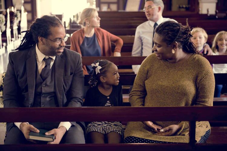 A mother and father who want to spark their child's relationship with God sitting on either side of a young girl in a church pew