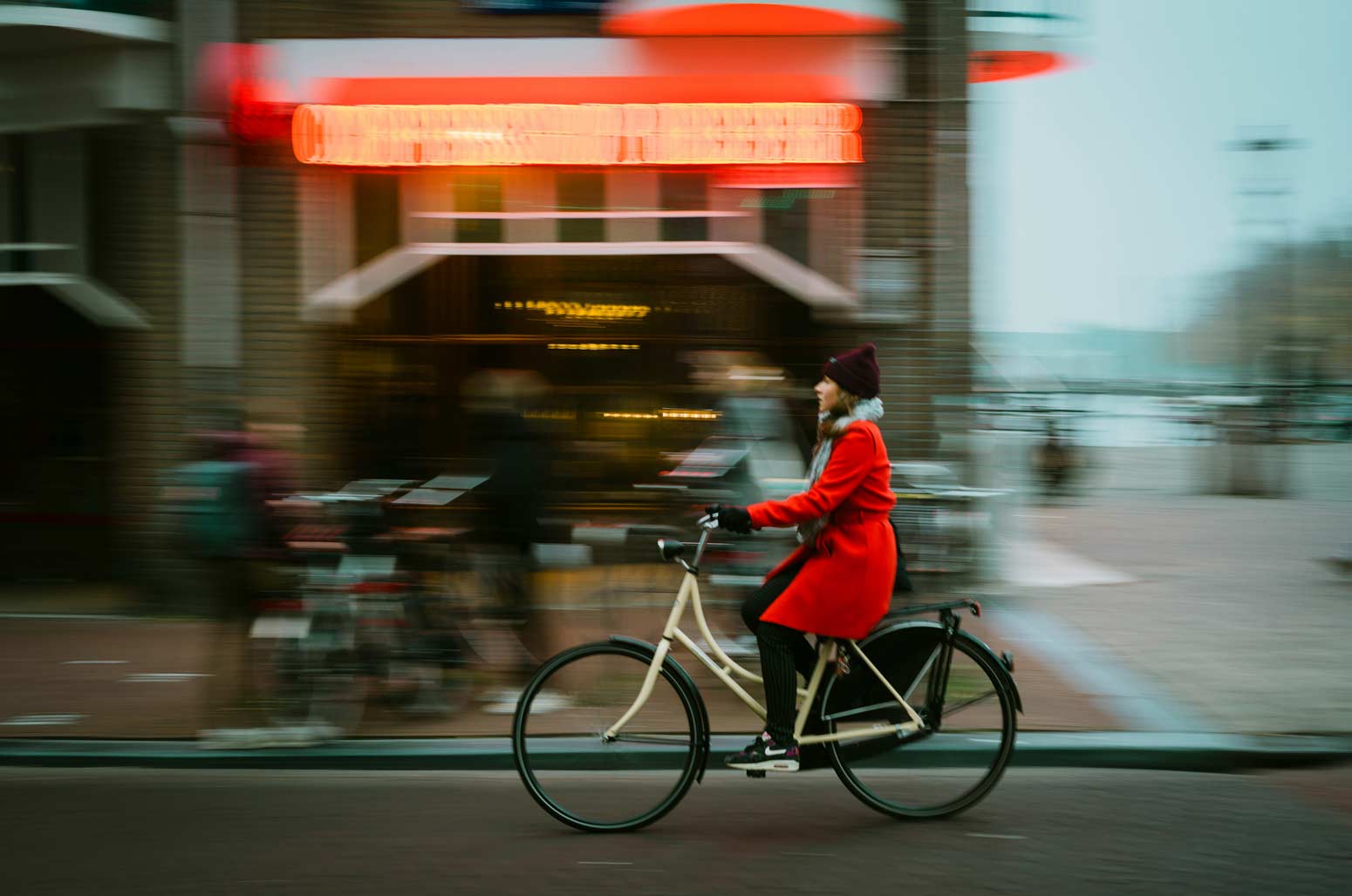 women wearing a red coat riding a bike in a city block and speeding through life