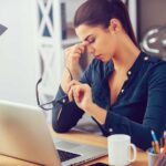 woman at a computer with her eyes closed and head in her hand wondering when to leave a job that's not serving her