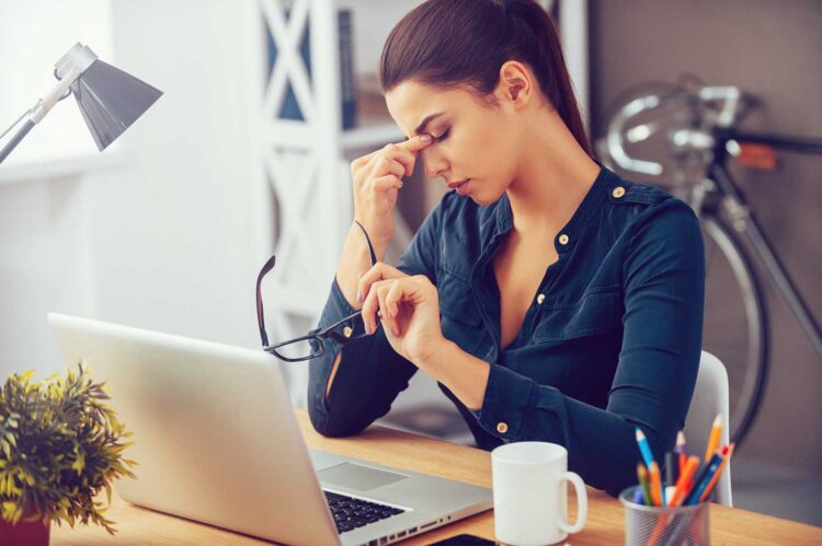 woman at a computer with her eyes closed and head in her hand wondering when to leave a job that's not serving her