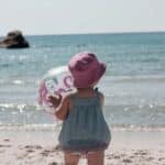 a little girl holding an inflatable ball at the beach, a moment that reminds every mom to soak up every minute with their kids